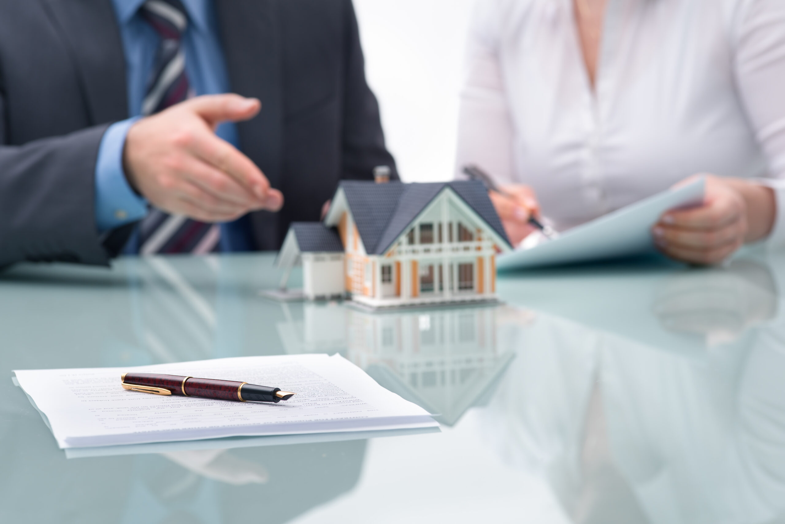 Business professionals discuss a housing agreement, with a model house and paperwork displayed on the table, highlighting real estate transactions.