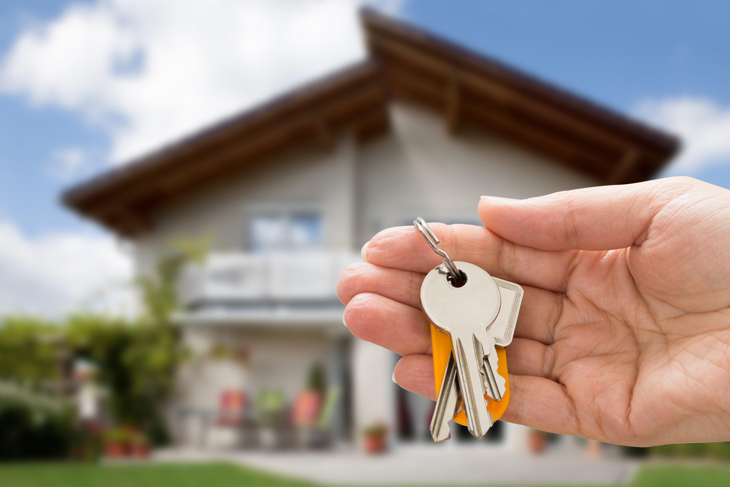 Hand holding house keys in front of a modern home. The image signifies new ownership and the excitement of moving into a new property.