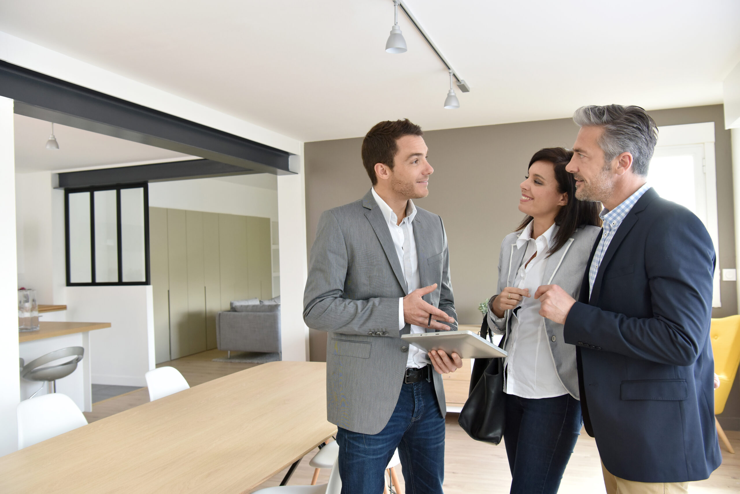 Real estate professionals engage with potential clients in a modern interior space, discussing property details and showcasing a collaborative atmosphere.