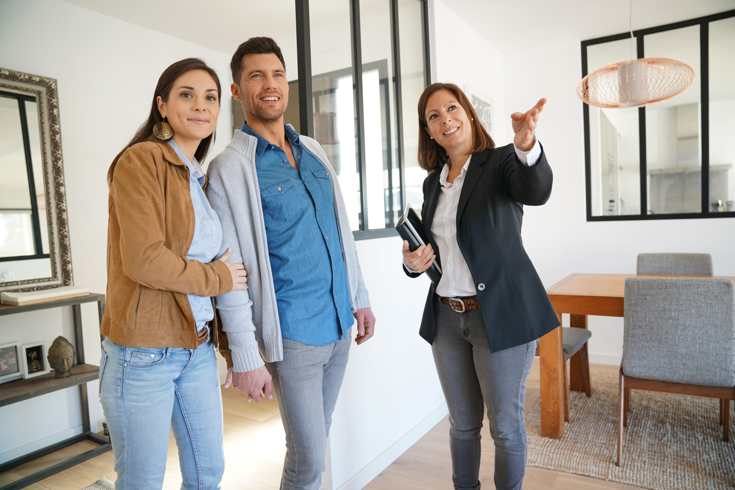 A real estate agent points out features to a couple in a bright, modern home, highlighting its appeal during a property showing.